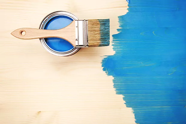 Ein Stück Spanplatte mit blauer Farbe und einem Pinsel